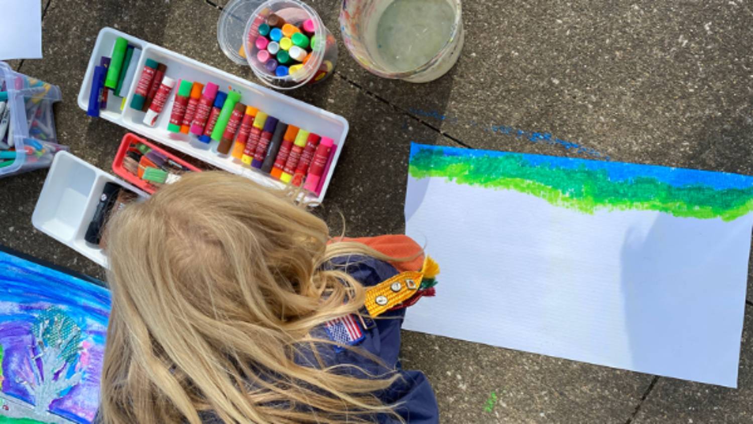 Young boy colors on the sidewalk with blue and green chalk