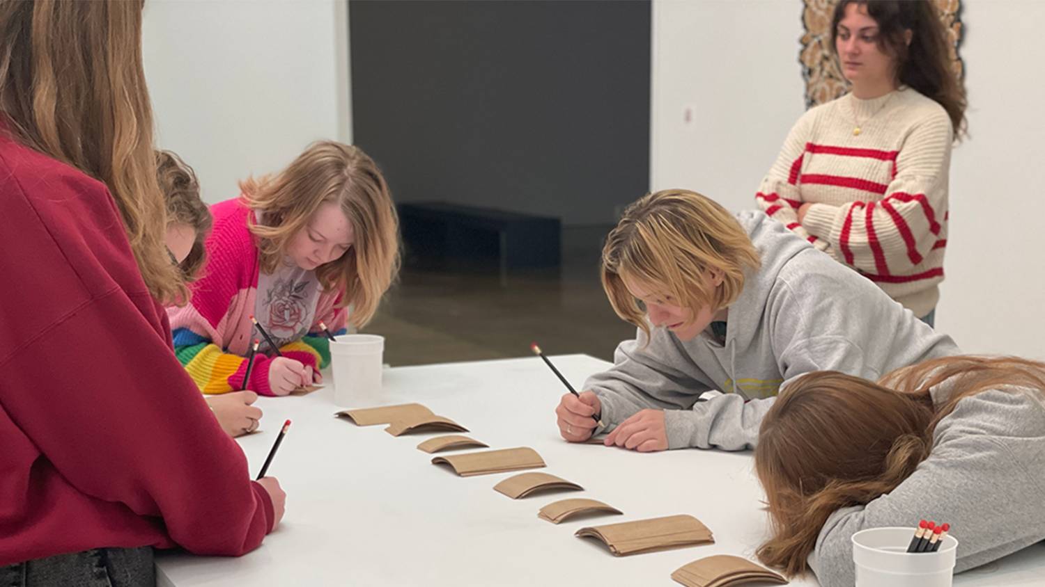 High school aged artist draw on an all white table supervised by art graduate students